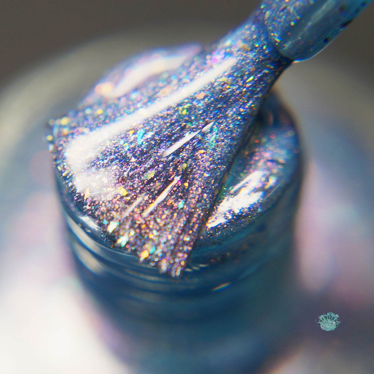 Close-up of a brush applying East of the Storm.029 Blue Nail Polish by PI Colors. The brush is covered in sparkly particles, showcasing a mix of pink and purple hues with color-shifting iridescent flakies. The glossy texture highlights the shimmering effect as it dips into the nail polish bottle.