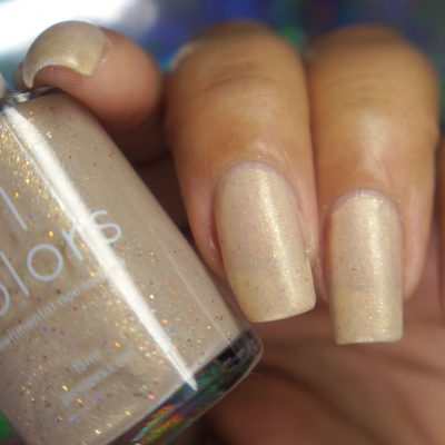 A close-up of a hand with neatly manicured nails painted in PI Colors' "Shark's Eye Moonshell.062" nude cream nail polish. The thumb holds the handmade bottle containing the same polish, which features holographic glitter particles for an elegant touch.