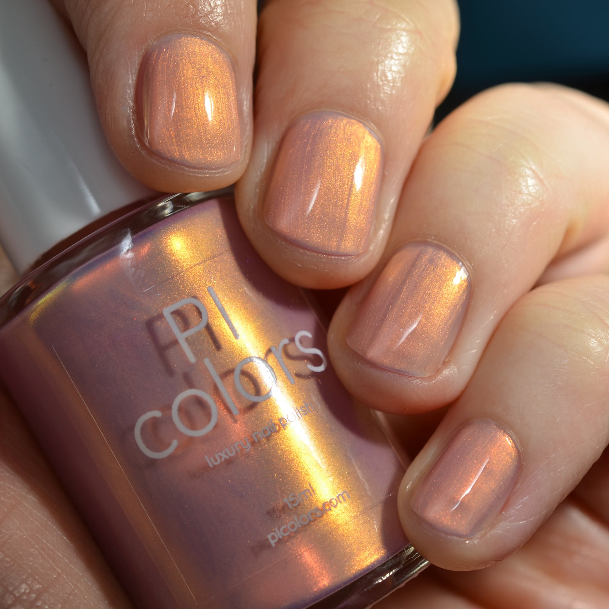 Hand holding a bottle of PI Colors nail polish with matching pink nail color
