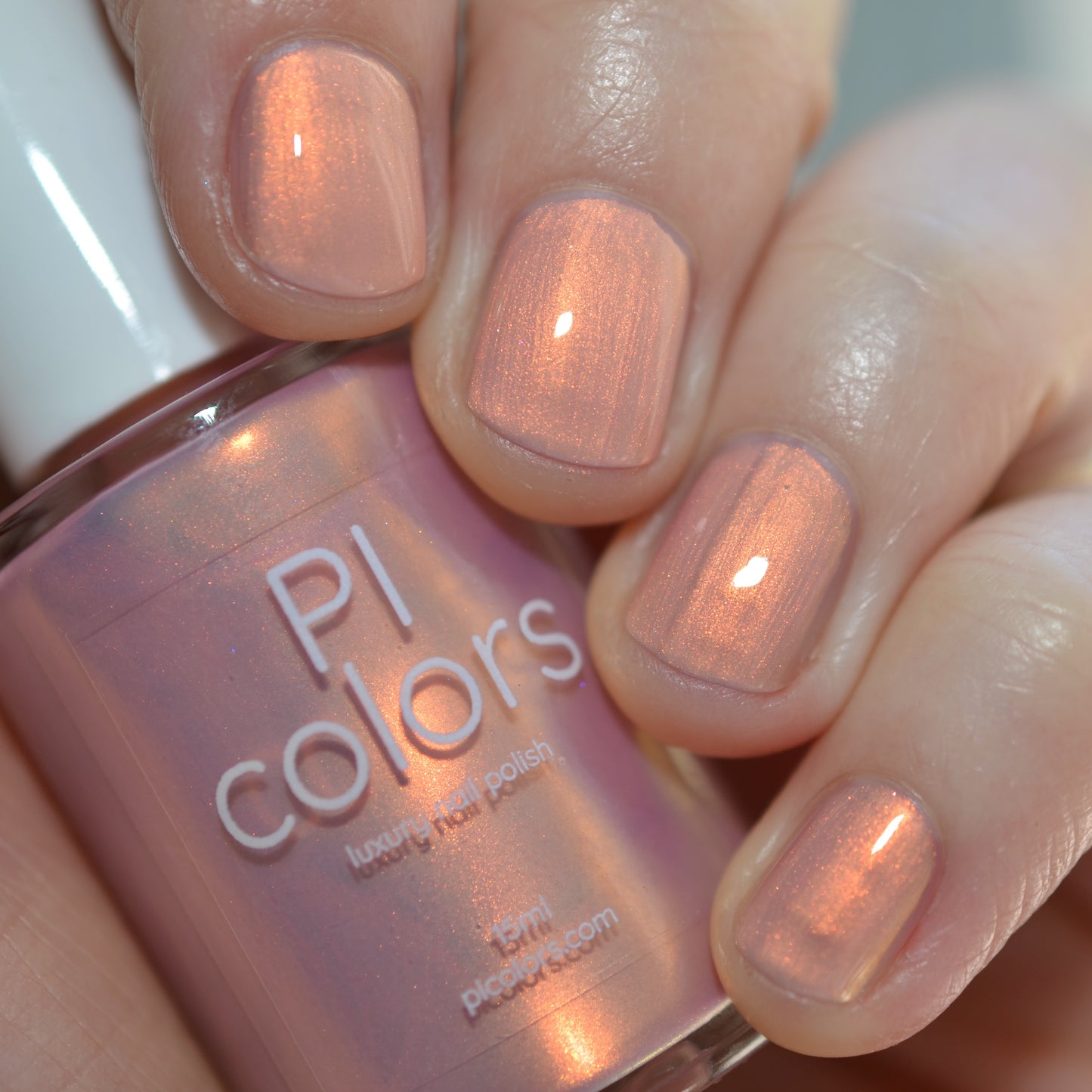 Hand holding a bottle of PI colors nail polish with matching pink nails.