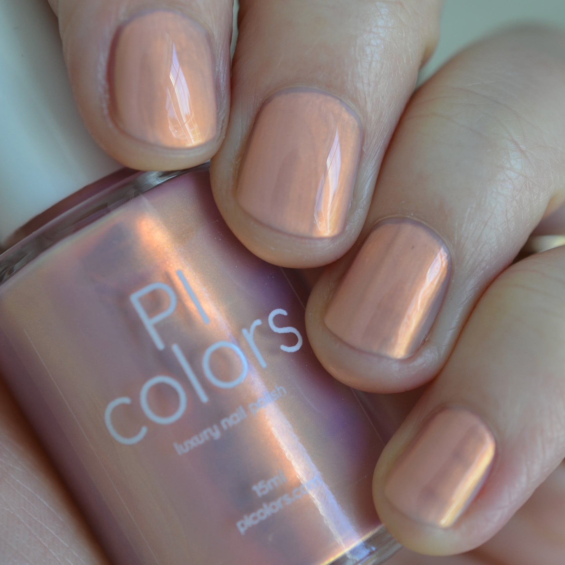 Hand holding a bottle of PI colors nail polish with matching pink nail color.