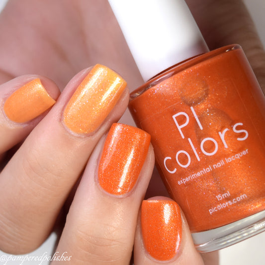 A hand with manicured nails, painted in a gradient of orange to yellow tones, holds a bottle of Sun Conure.097 Orange Nail Polish by PI Colors. The shimmery bright orange shade enhances its elegance, showcasing the allure only a true 10-free polish can provide.