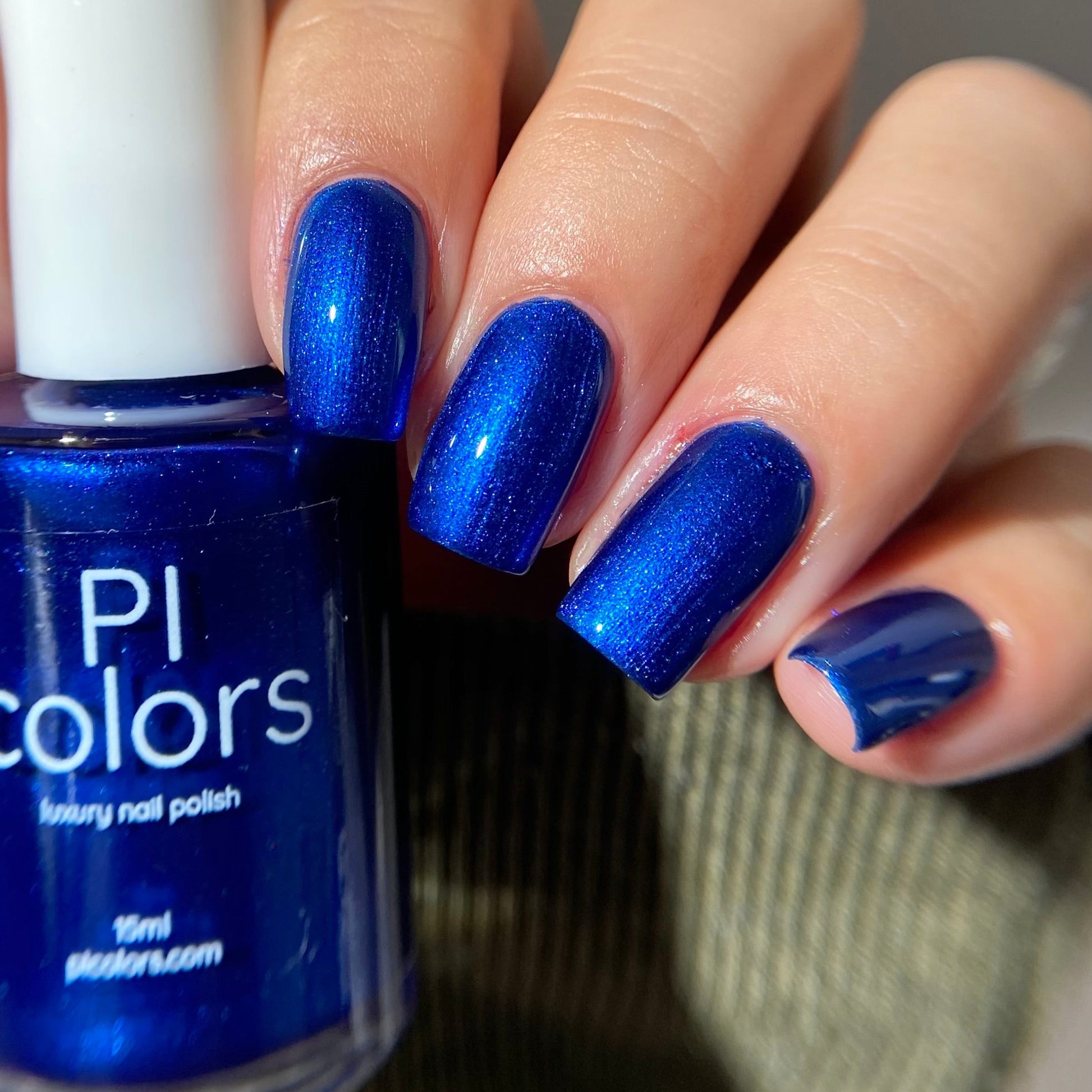 Blue nail polish with a hand displaying matching nails against a neutral background