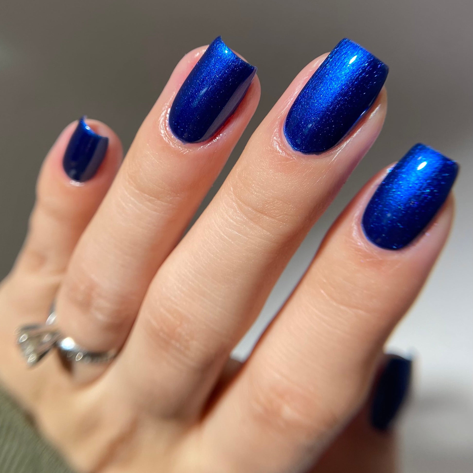 Hand with blue glittery nail polish on a neutral background