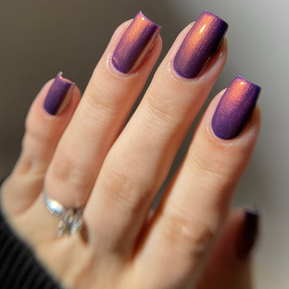 Hand with purple nail polish on a neutral background