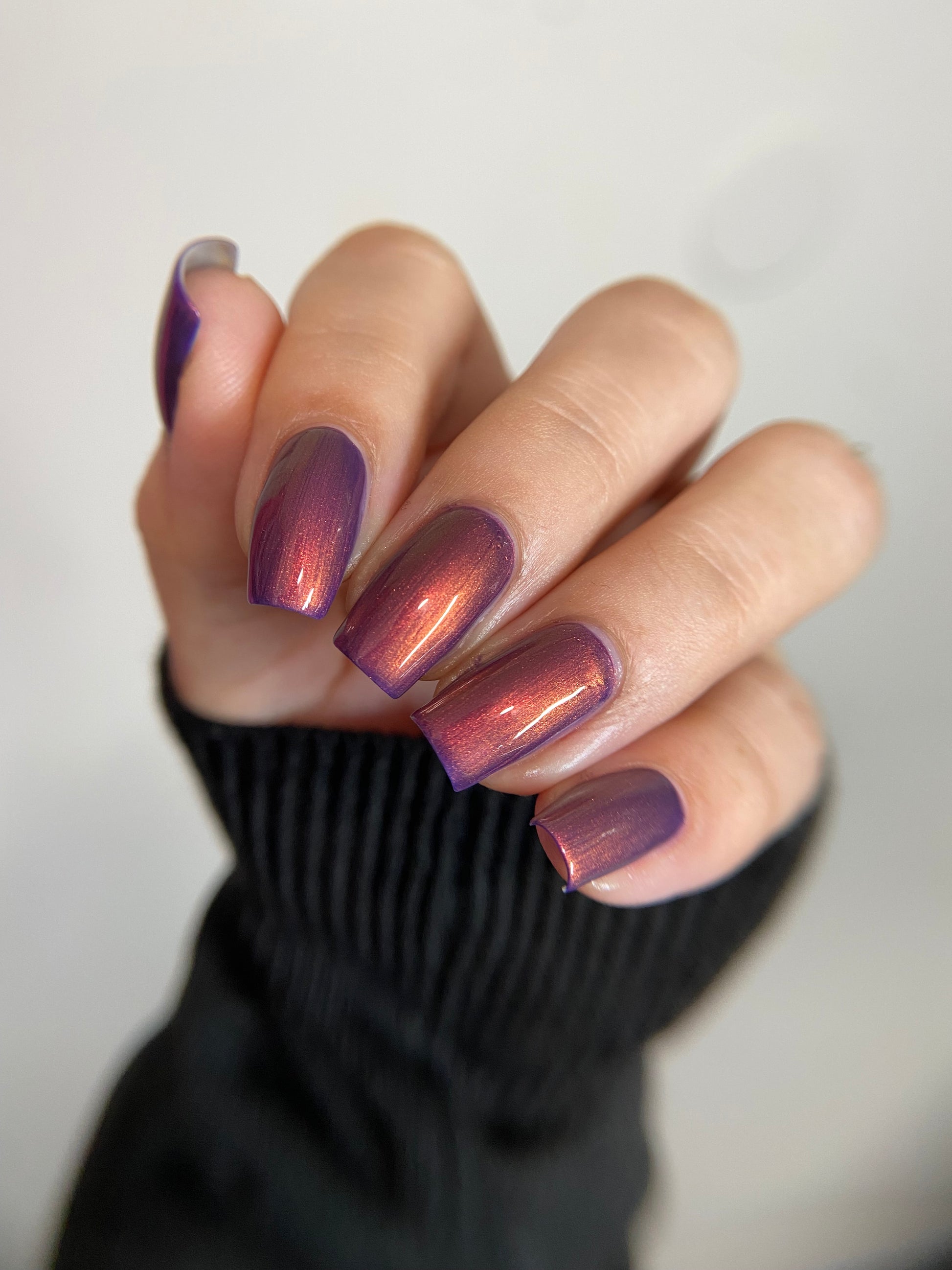 Hand with purple nail polish on a neutral background