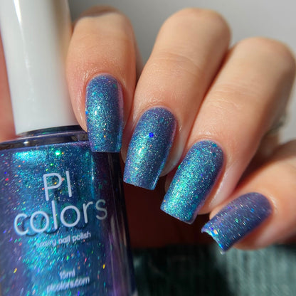 Hand with blue glittery nail polish holding a bottle of PI Colors nail polish.