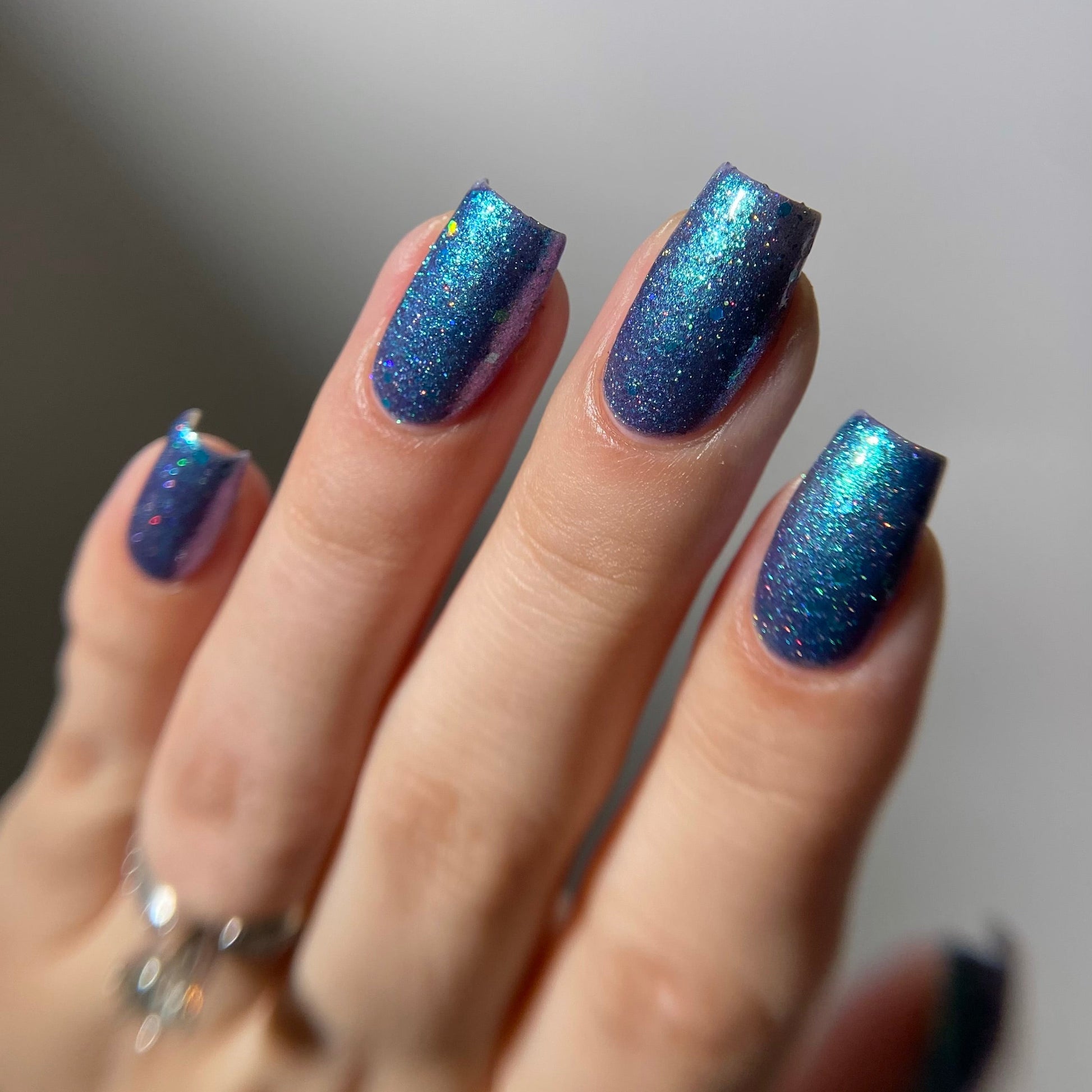 Hand with blue glittery nail polish on a neutral background