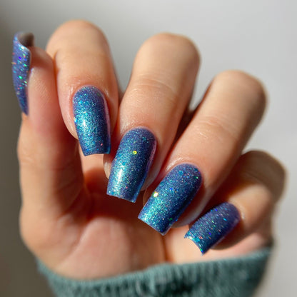 Hand with blue glittery nail polish on a plain background