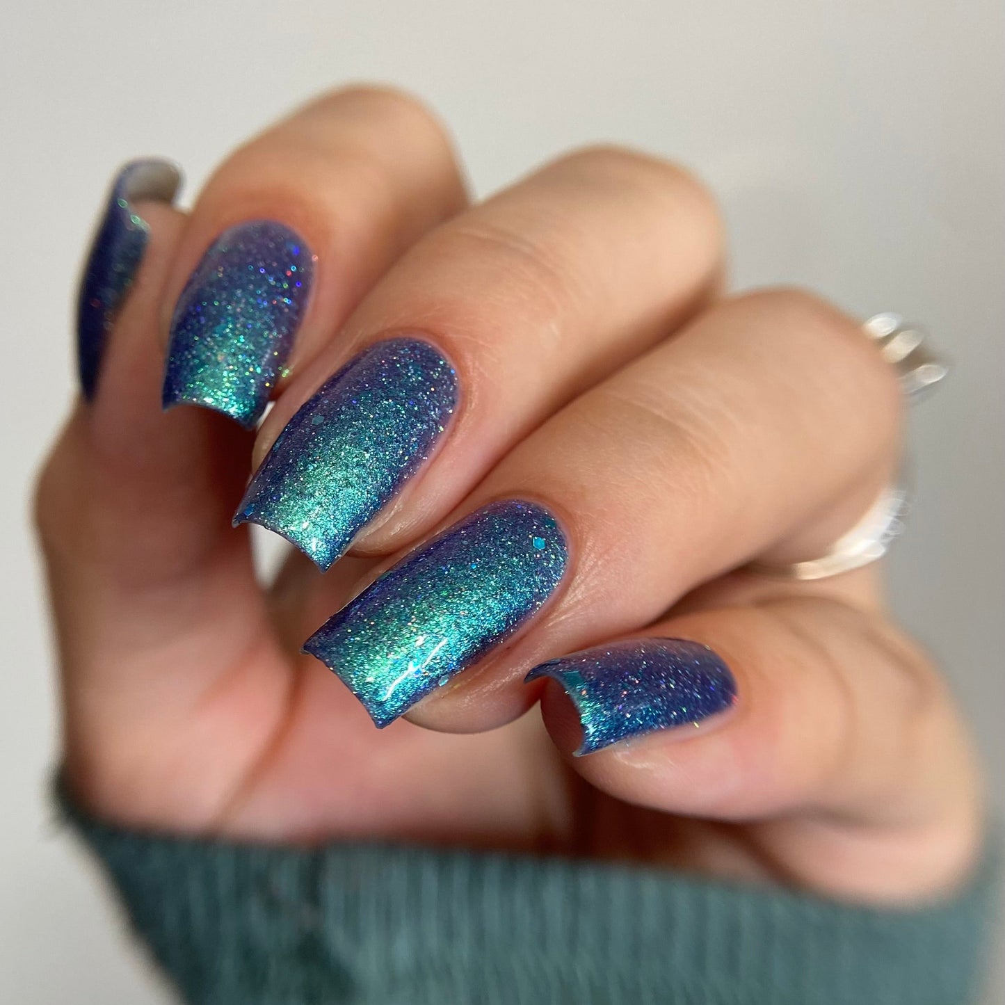Hand with blue and green glittery nail polish on a plain background
