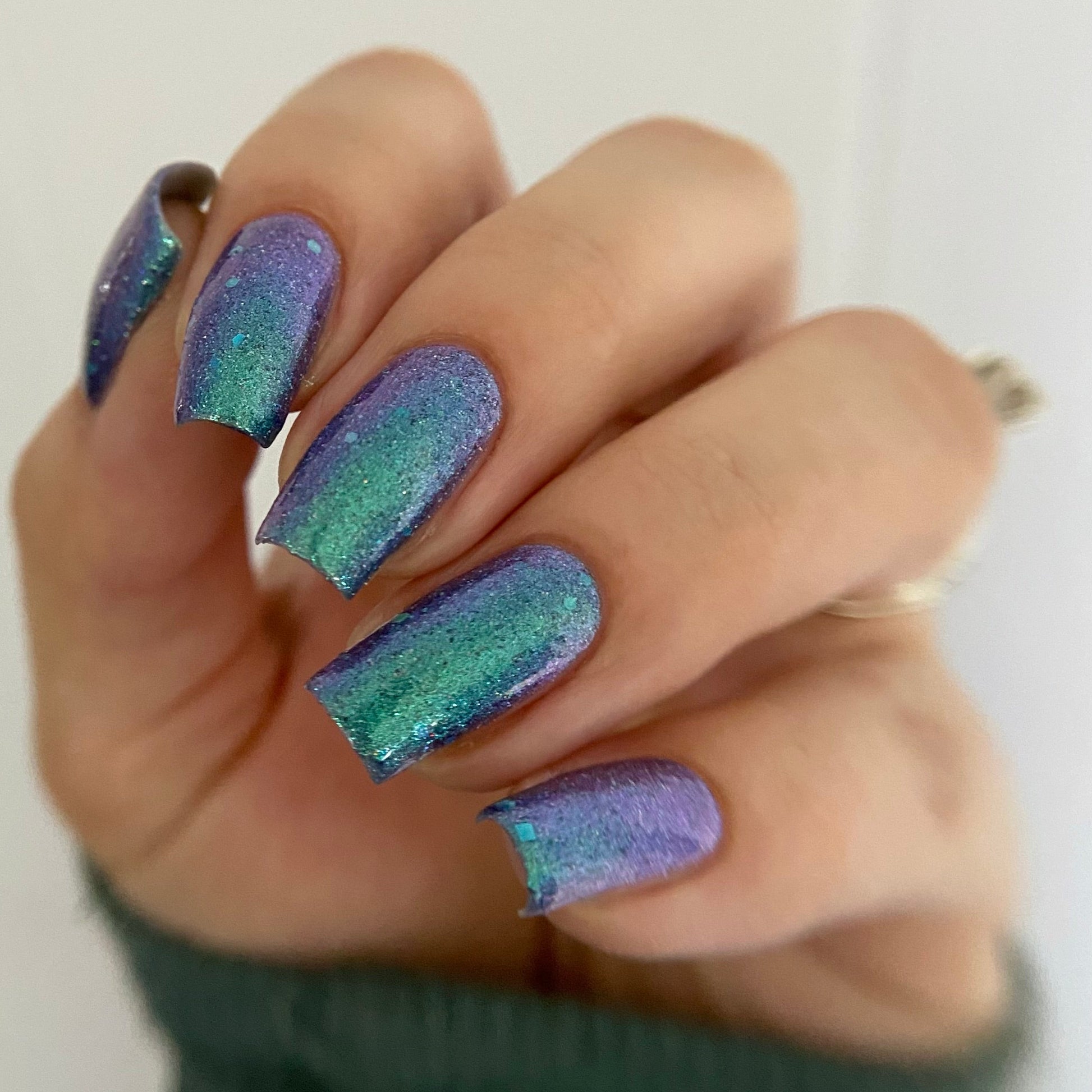 Hand with purple and green gradient nail polish on a plain background