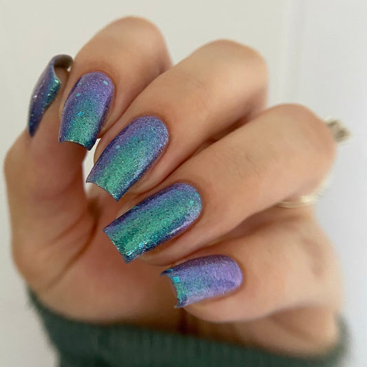 Hand with purple and green gradient nail polish on a plain background