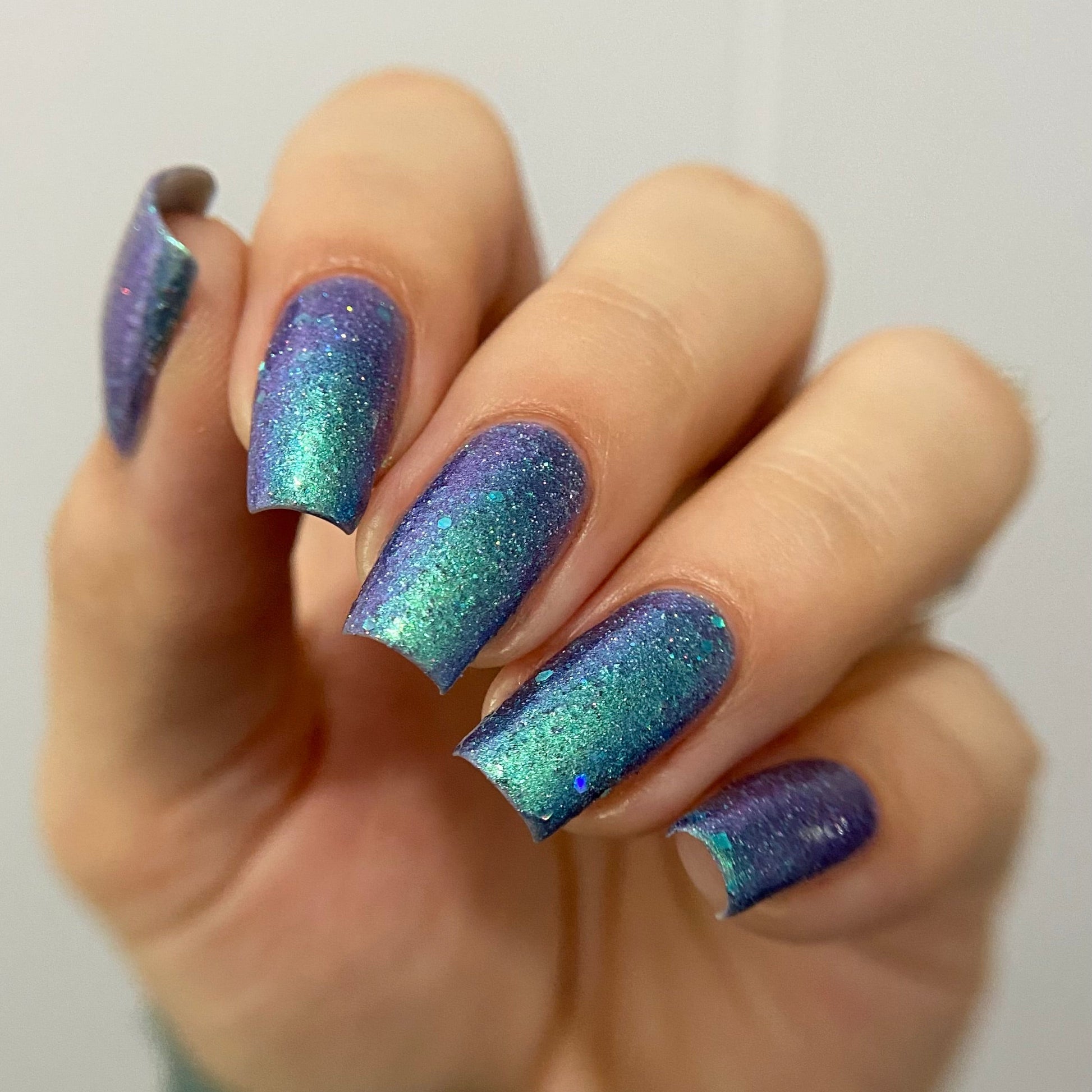 Hand with blue and purple glittery nail polish on a plain background