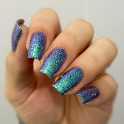 Hand with blue and purple glittery nail polish on a plain background