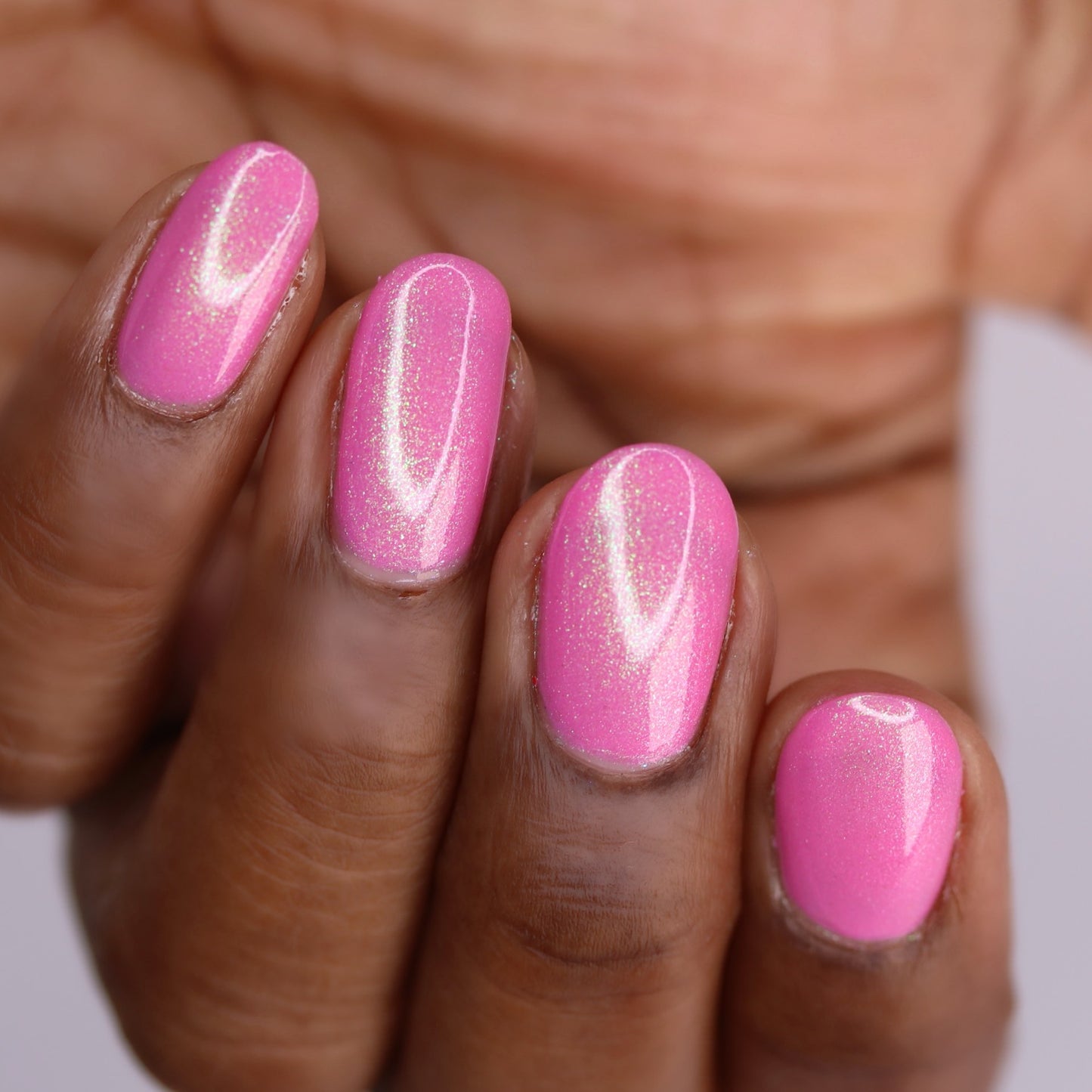 A close-up of a hand with neatly manicured nails painted in PI Colors Mint and Summer.100, a glossy, fluorescent pink polish with vibrant colorshifting shimmer.