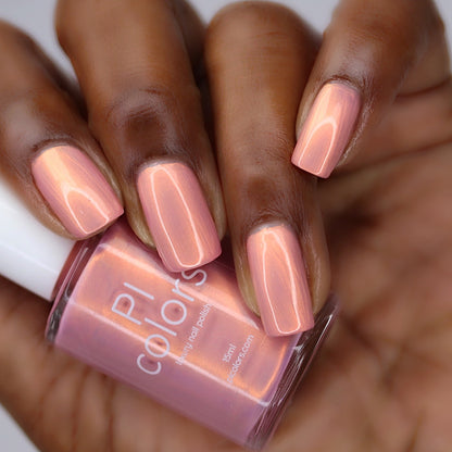 Pink nail polish bottle with a hand displaying pink nails against a blurred background