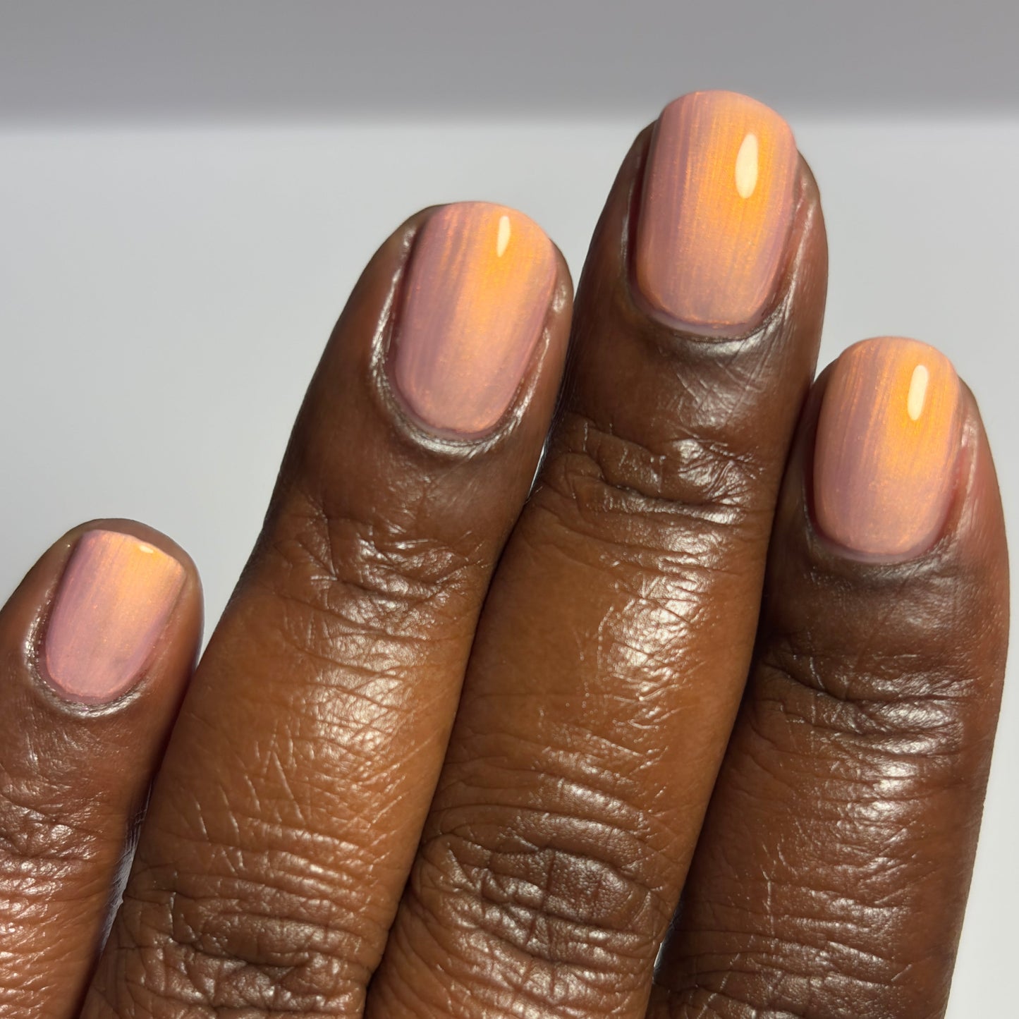 Close-up of a hand with pink nail polish on a neutral background