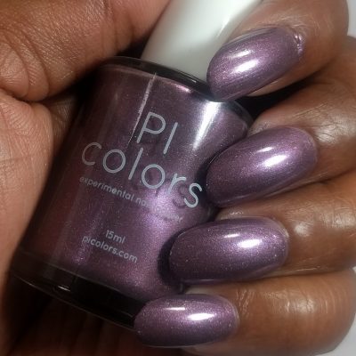 A hand with shimmering plum nail polish holds a bottle of "Cœur.005 Purple Nail Polish" by PI Colors, showcasing its exquisite blend of handcrafted beauty.