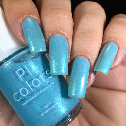 A close-up captures a hand adorned with long, glossy aqua blue nails accentuated by holographic powder. The person holds a bottle of PI Colors nail polish labeled "Berry Mousse.001 Blue Nail Polish," with the shimmer effect on the polish perfectly complementing the vibrant color of the nails.