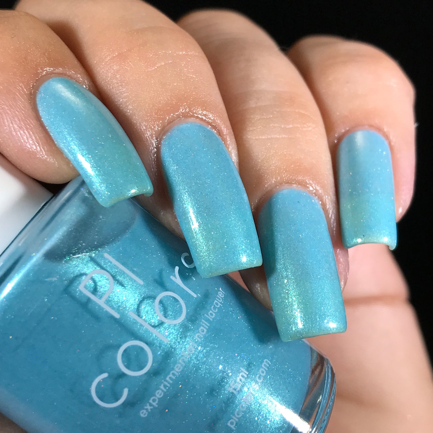 A hand showcases long, glossy nails painted in a stunning shade of Berry Mousse.001, a dazzling aqua blue with holographic powder that creates subtle color shifts in the light. The "PI Colors" bottle, which is 10-free and complements the vibrant hue, is perfectly nestled between the fingers.