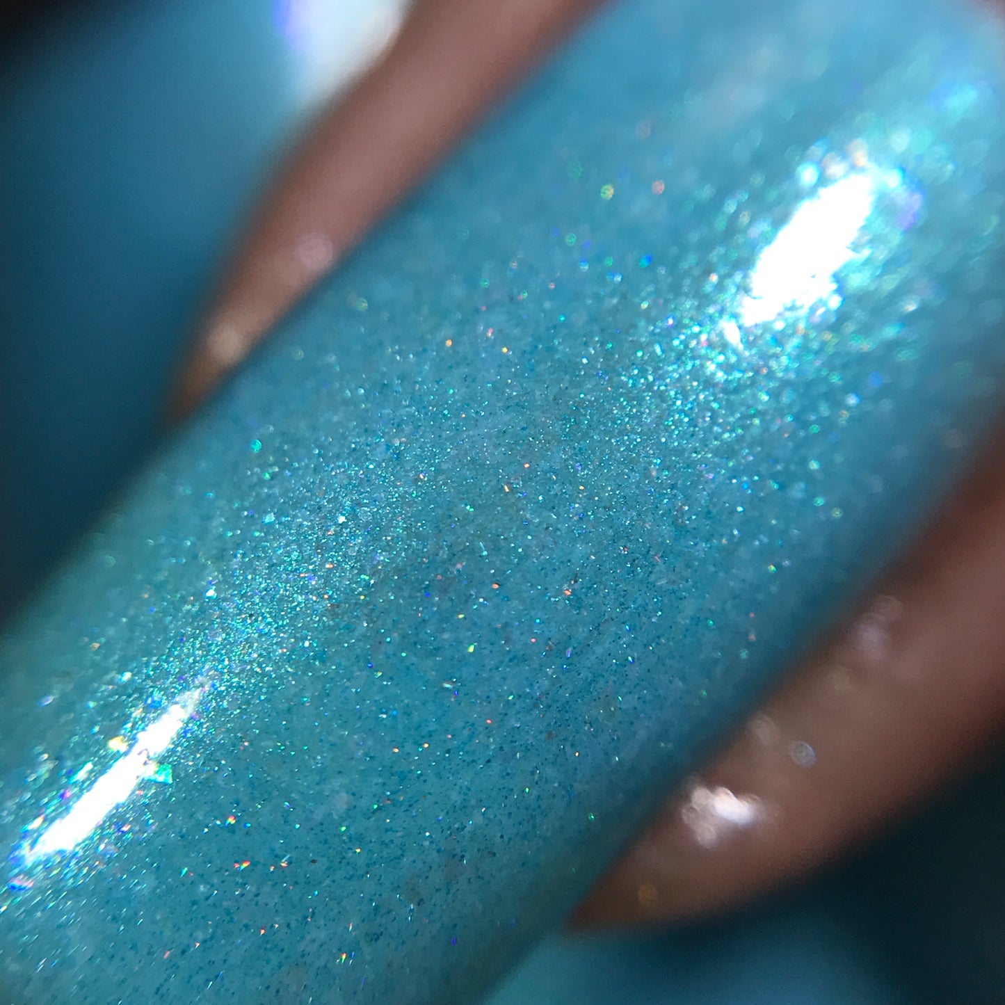 Close-up of a fingernail painted with PI Colors' Berry Mousse.001 Blue Nail Polish. Enhanced by holographic powder, this 10-free shimmering turquoise polish features tiny sparkles and reflects light, giving it a glossy appearance.