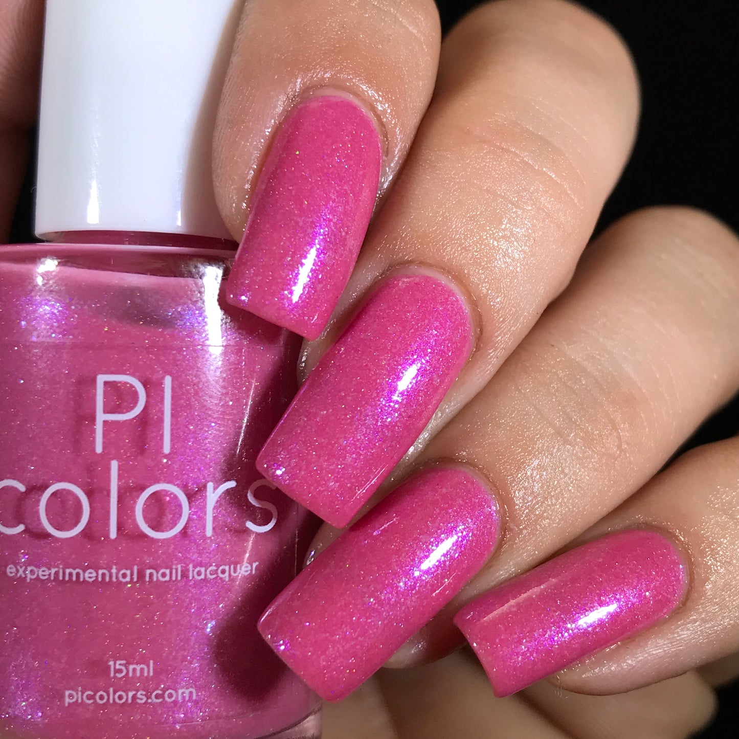 A close-up of a hand with long nails adorned in a shimmering bright pink nail polish, infused with holographic powder, reveals a captivating look. The bottle of polish, labeled "PI Colors" and "Strawberry Sundae.002," is elegantly held in hand, featuring the website "picolors.com" and described as an experimental nail lacquer.