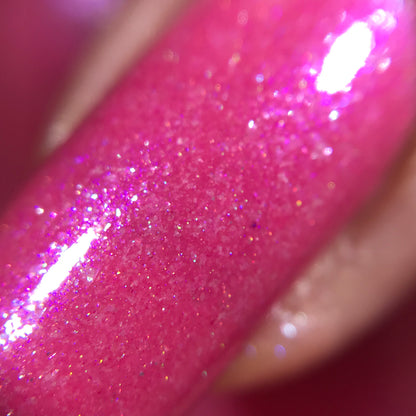 A close-up of the PI Colors Strawberry Sundae.002 Pink Nail Polish showcases its pink glittery finish on a fingernail, infused with holographic powder for added brilliance. The glossy, shimmering surface dazzles with tiny sparkles reflecting light, while its smooth texture accentuates the richness of the metallic pink hue.