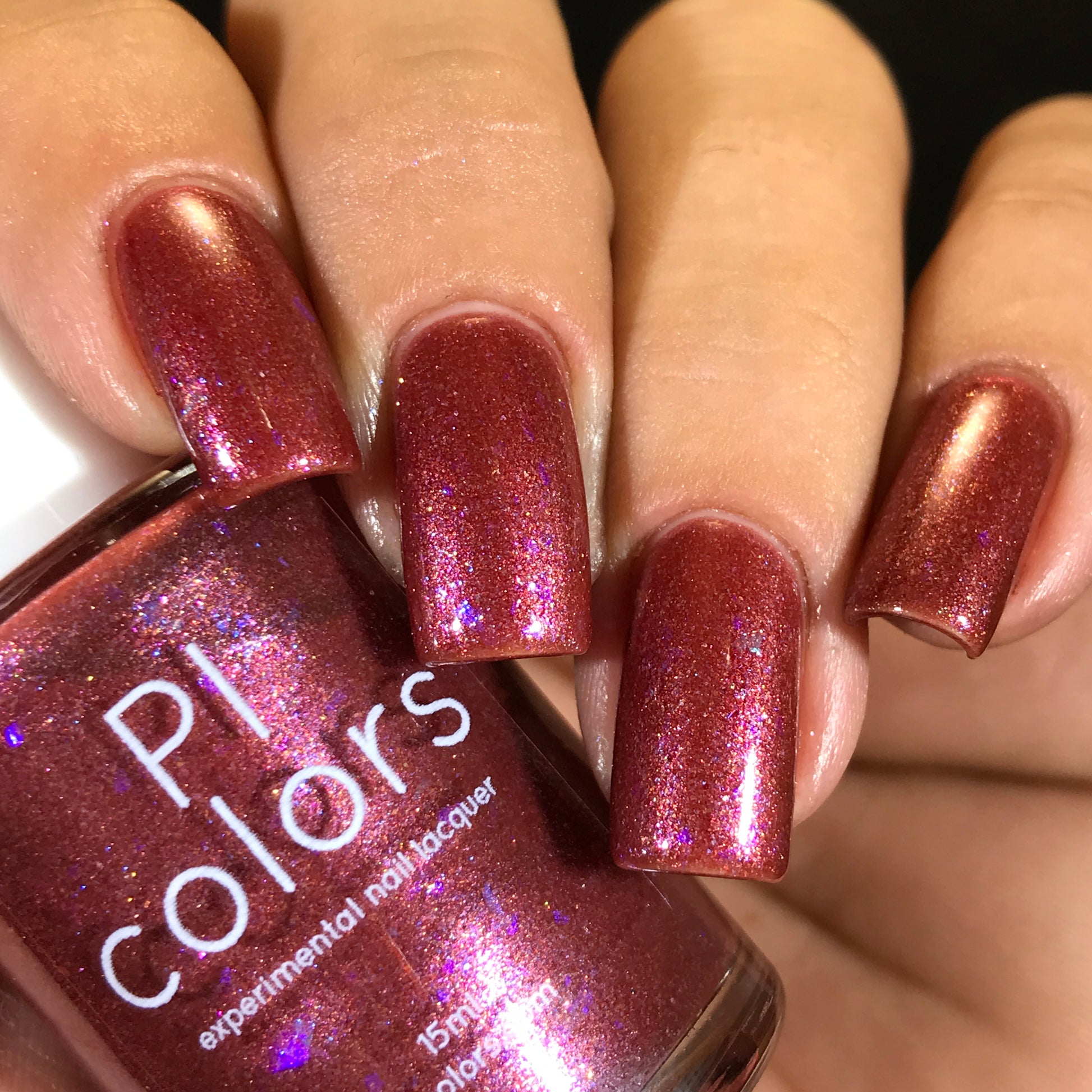 A close-up shot captures a hand with nails painted in a shimmering, luxurious shade of red from PI Colors. The bottle labeled "Quasar.156 Red Nail Polish" is held next to the nails, highlighting the same dramatic color-shifting flakies and glittery finish.