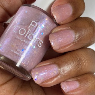 A hand with neatly manicured nails painted in a shimmery pink hue holds a bottle labeled "Special Week.000 Pink Nail Polish" by PI Colors, highlighting the elegance of handcrafted nail polish.