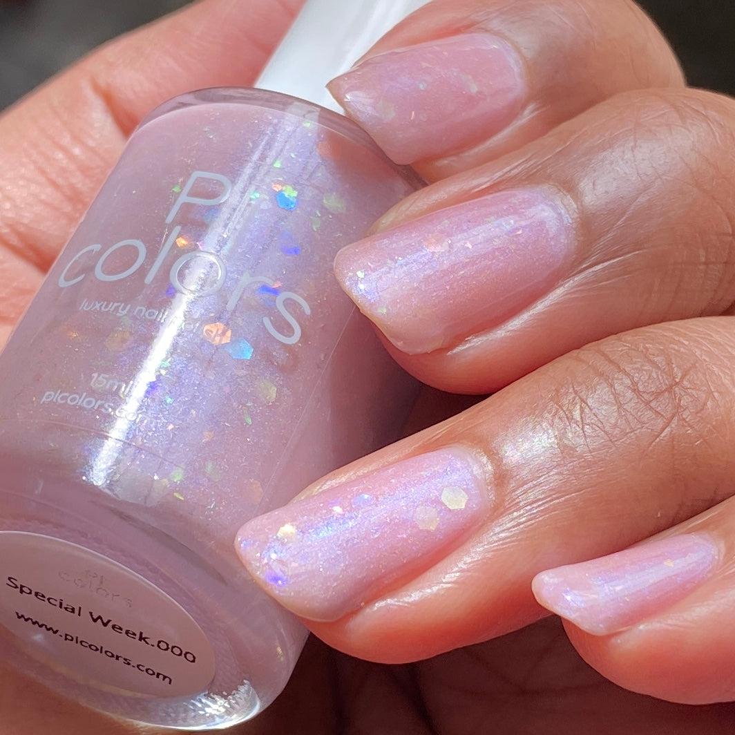 A hand with long nails painted in Special Week.000 Pink Nail Polish, a luxurious pale pink shade with holographic flakes. The person is holding the bottle of the same polish labeled "PI Colors," showcasing its subtle iridescent effect in sunlight.