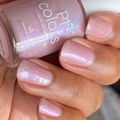 A hand with impeccably manicured nails, adorned in the shimmering shade of Special Week.000 Pink Nail Polish, elegantly holds a bottle labeled “PI Colors.” This handmade polish features a delicate glittery effect that enhances your look with a refined elegance.