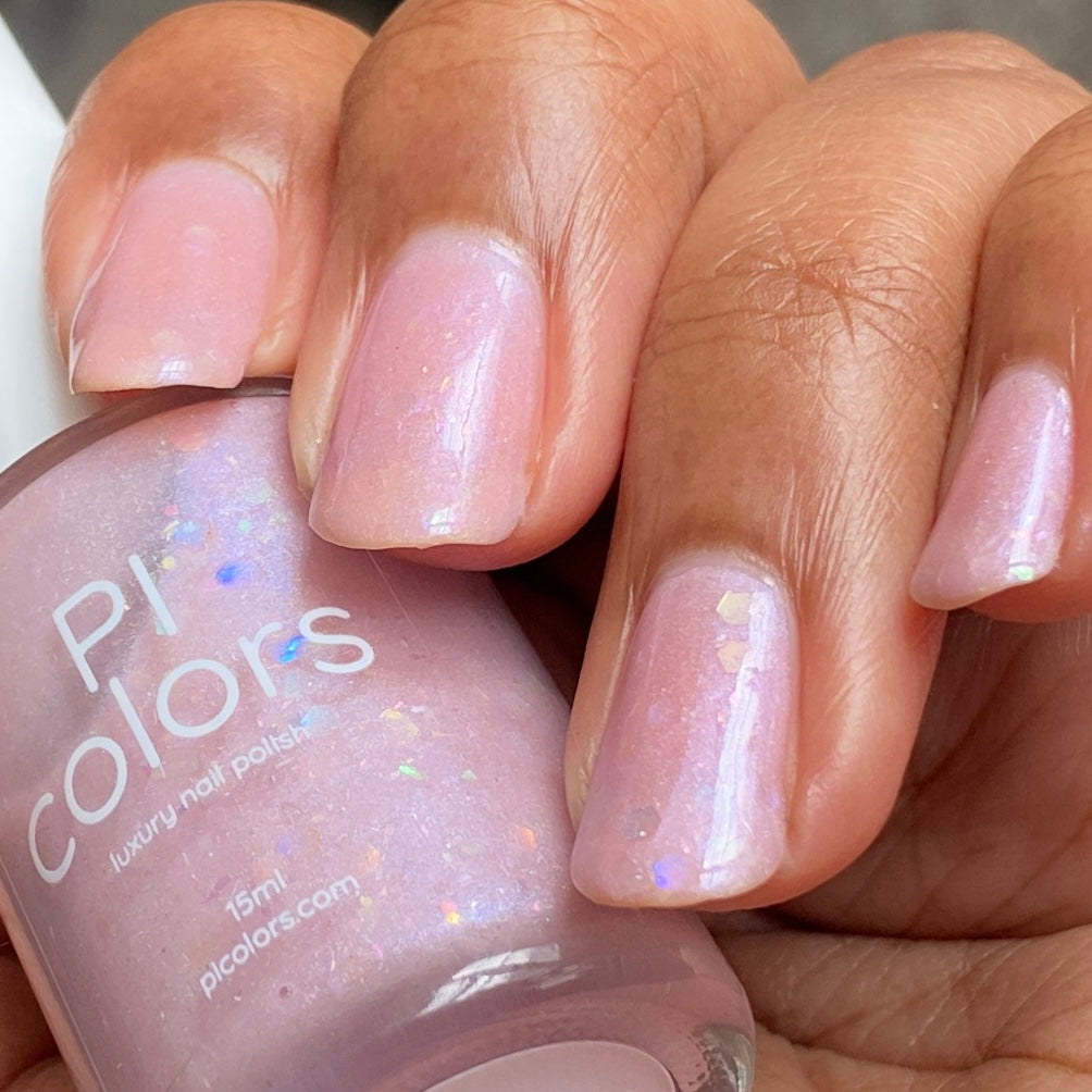 Close-up of a hand with light pink, iridescent luxury nail lacquer, holding a bottle labeled "PI Colors Special Week.000 Pink Nail Polish, 15ml, picolors.com." The polish boasts a subtle shimmer with tiny reflective specks perfect for any Uma Musume Pretty Derby fan.