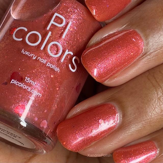 A close-up of a hand features nails painted with a shimmering pink-orange shade of "Strawberry Jam.228 Red Nail Polish" by PI Colors. The bottle displays the same color, highlighting the 10-free nail lacquer's glossy and sparkling texture for a stunning, vibrant look.