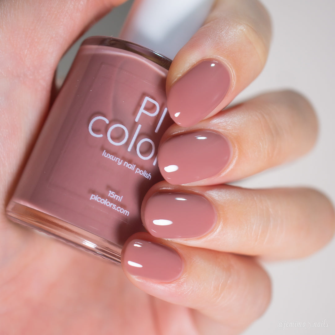 A hand with neatly manicured nails painted in a glossy, mauve pink shade holds a matching bottle of PI Colors Iced Oatmeal.478 10-free handmade nail polish.