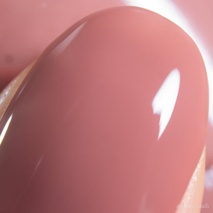 A close-up of a single fingernail painted with PI Colors Iced Oatmeal.478, a glossy, light mauve-pink 10-free nail polish, reflecting light and showing a smooth, shiny finish.