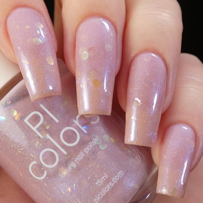 A close-up shows fingers with long nails adorned in a shimmery, light pink polish featuring holographic flakes. A bottle labeled "Special Week.000 Pink Nail Polish" by PI Colors is held prominently in the foreground, highlighting luxury nail lacquers that perfectly complement the dazzling nails.