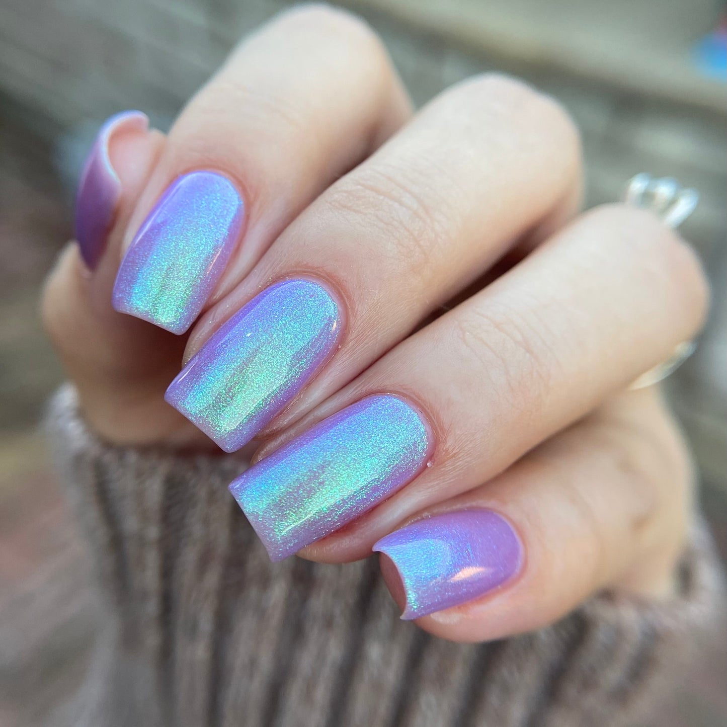 Hand with iridescent purple nail polish on a blurred background