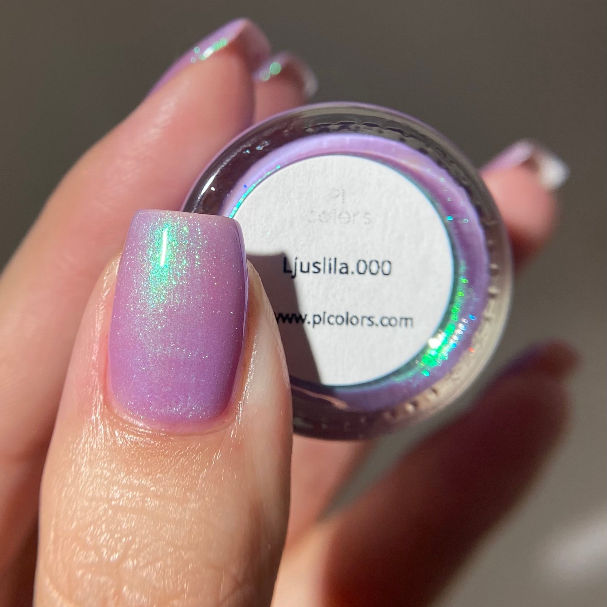 Nail polish jar with a hand displaying a similar purple glittery nail color.