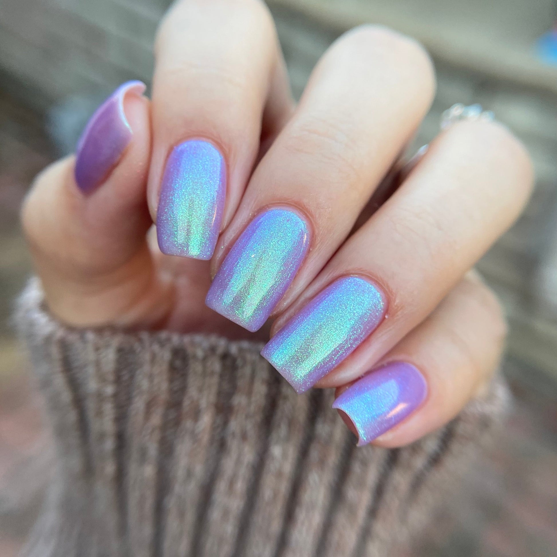 Hand with purple and iridescent nails against a blurred background