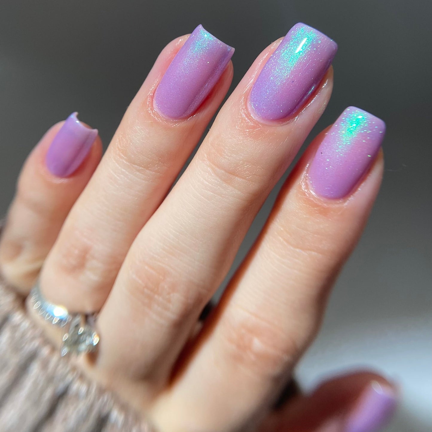 Hand with purple glittery nails against a neutral background