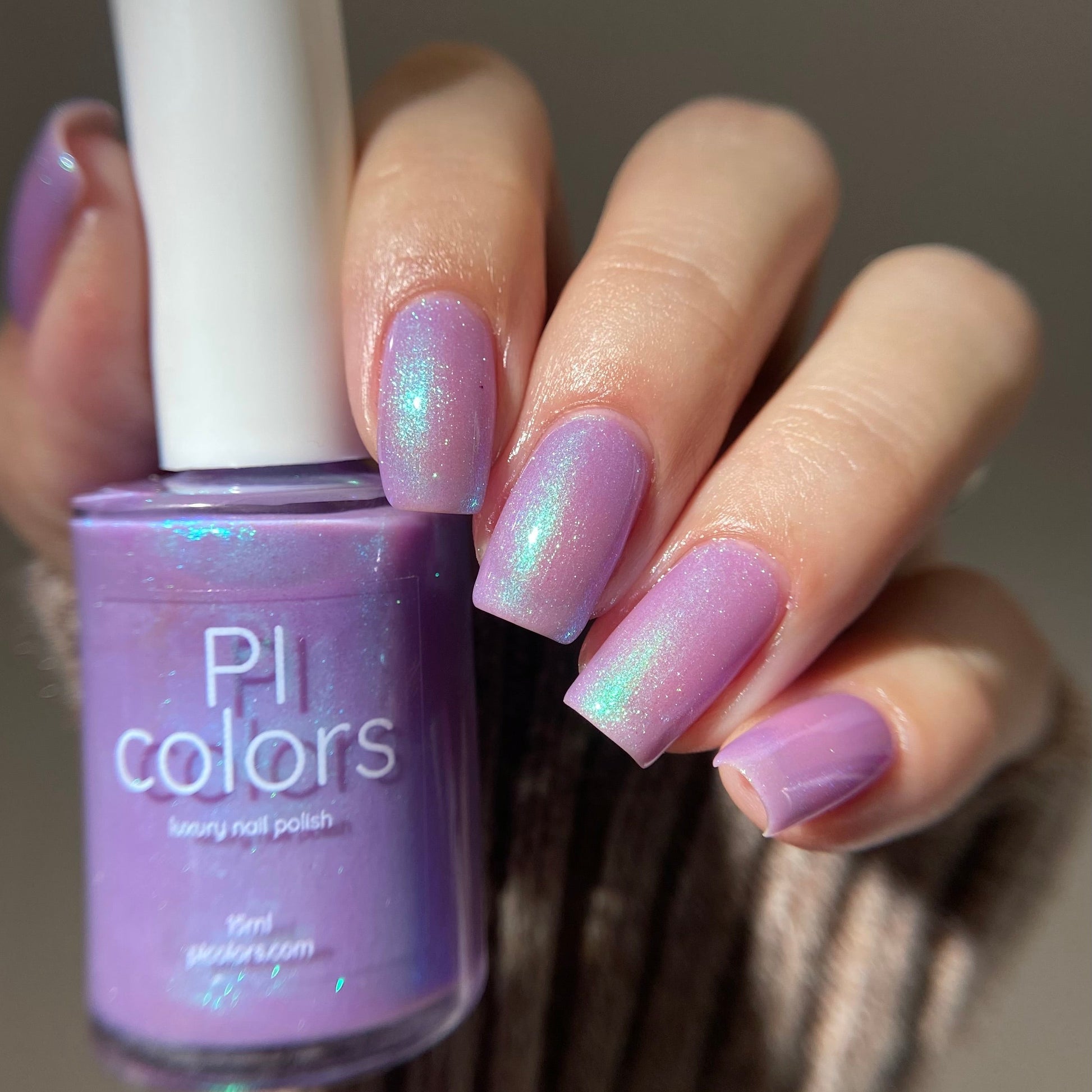 Hand holding a bottle of purple nail polish with matching nails against a neutral background
