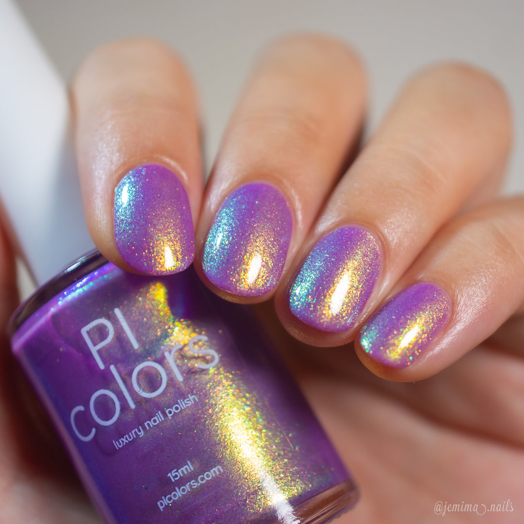 A close-up of a hand with nails painted in an iridescent purple nail polish with gold shimmer, holding a bottle of PI colors luxury nail polish.