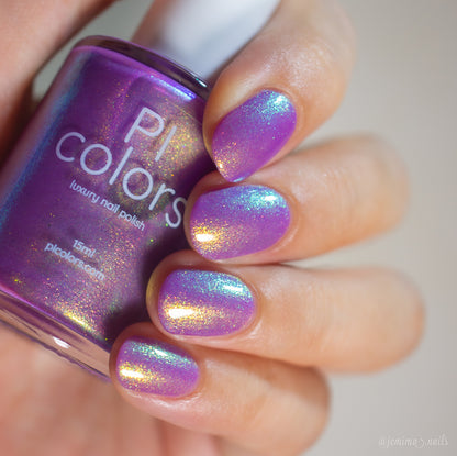 A close-up of a hand with nails painted in a holographic purple nail polish, holding a bottle of Pi Colors Luxury Nail Polish.