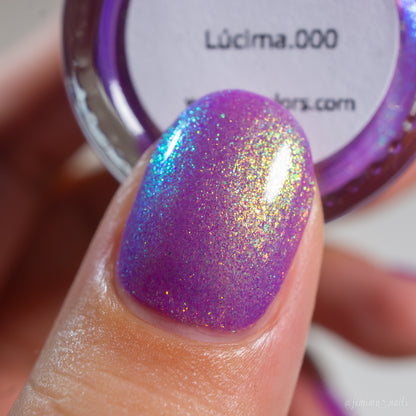 A close-up of a fingernail painted with a sparkling holographic purple nail polish, with a small open jar of the same polish in the background. The label reads 'Lüi.