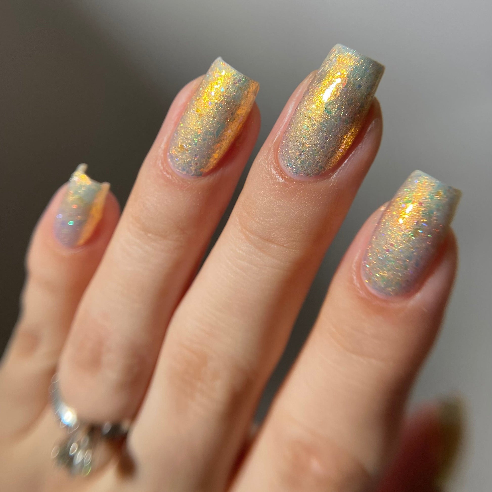 Hand with glittery nail polish on a neutral background