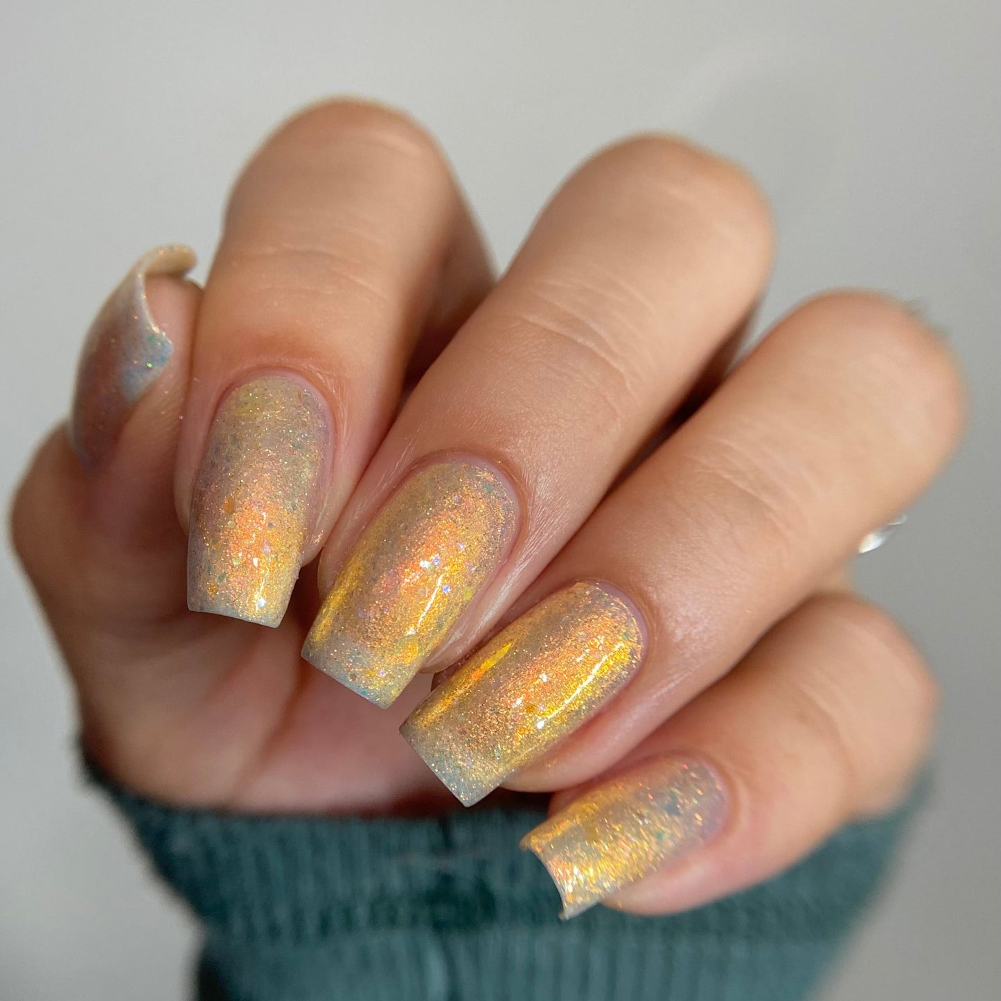 Close-up of a hand with glittery nail polish on a neutral background