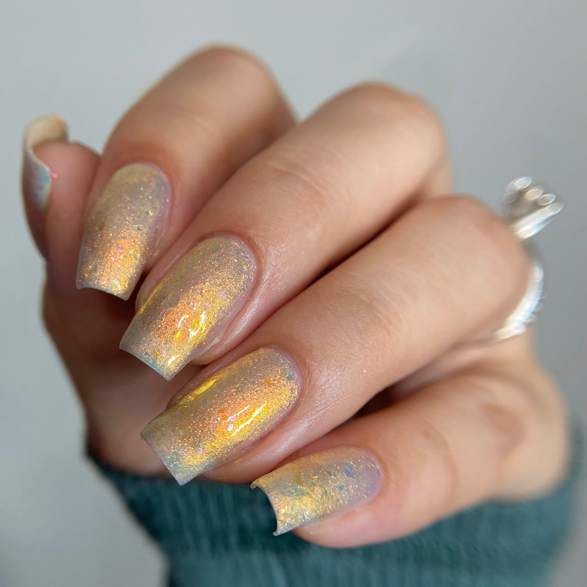 Hand with glittery nail polish on a neutral background