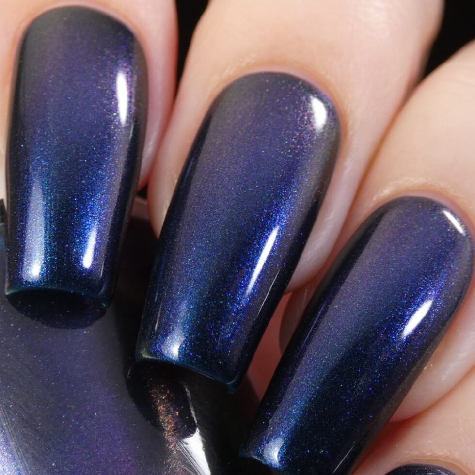 A close-up of fingers adorned with PI Colors' "Judge None Choose One.000" shows off a long, glossy dark blue nail polish with a multichrome finish. The shimmering effect catches the light, enhancing their smooth texture and bringing a hint of 90s nostalgia to life.