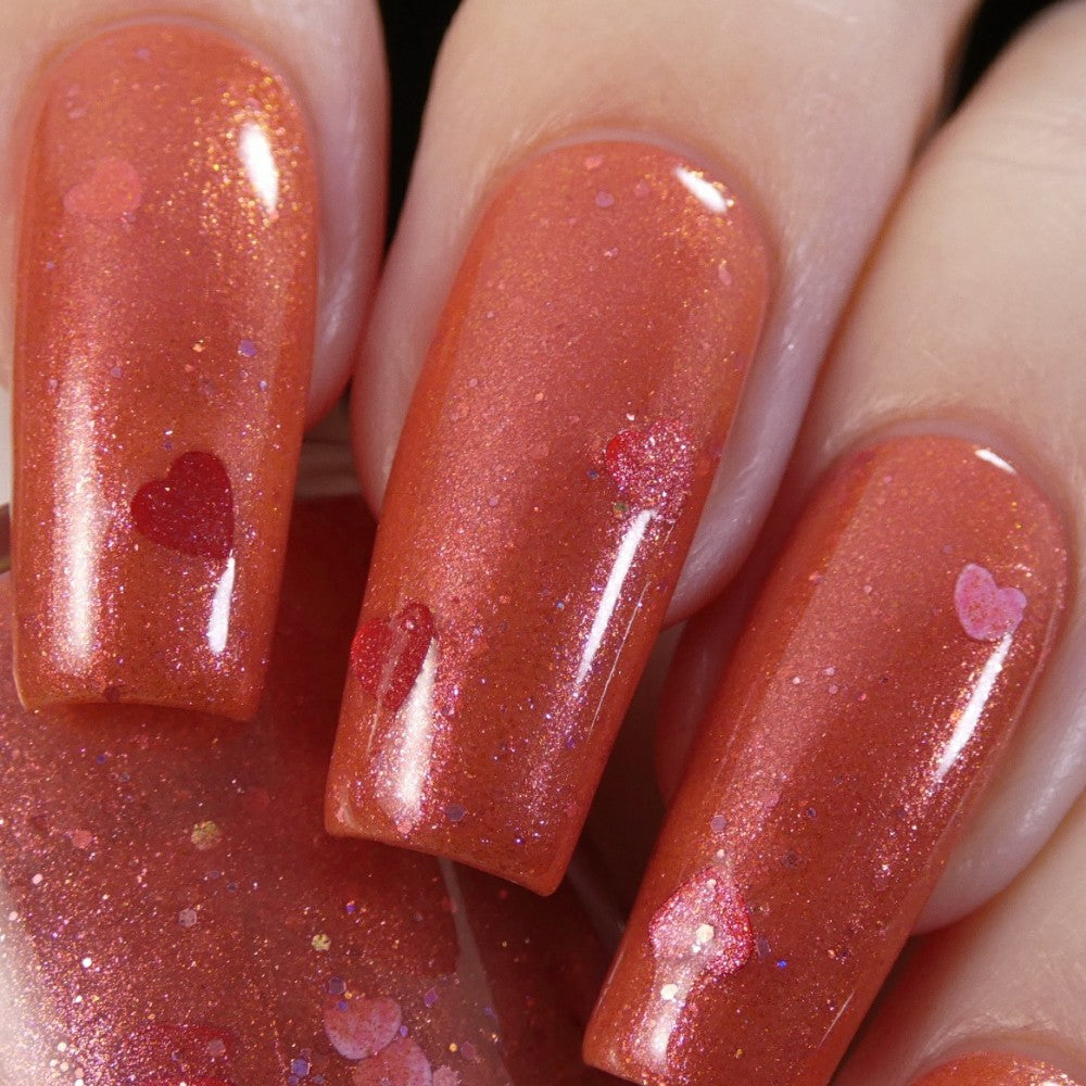 Close-up of fingers adorned with PI Colors' Strawberry Jam.228 Red Nail Polish, featuring shiny orange nail polish with small heart-shaped accents. The glossy finish is enhanced by a hint of red glitter, adding a playful and luxurious touch to the design.