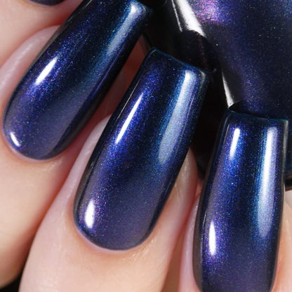 A close-up view showcases fingers adorned with long, glossy nails painted in PI Colors' "Judge None Choose One.000" Luxury Nail Lacquer. The multichrome finish offers iridescent hints of purple, delivering a dynamic effect under lighting that evokes 90s nostalgia.